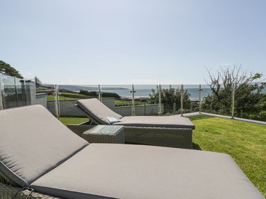 An outdoor terrace with two cushioned lounge chairs and a small table overlooking a grassy area and the sea at Melin Y Plas in Llanaber
