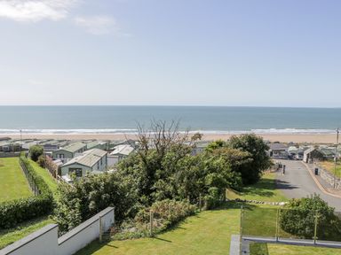 A view of green caravans near a beach with the sea and sky in the background at Melin Y Plas in Llanaber