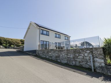 A two story house with solar panels on the roof and glass balcony fencing at Melin Y Plas in Llanaber