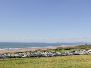 A coastal view with green fields beach and static caravans at Melin Y Plas in Llanaber