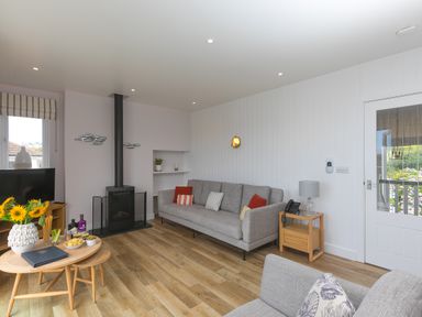 A living room with sofas a wood stove a television on a wooden stand and a table with flowers at Rowena in Mullion