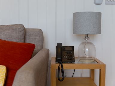 A side table with a telephone and a glass lamp next to a gray sofa with red and yellow cushions at Rowena in Mullion