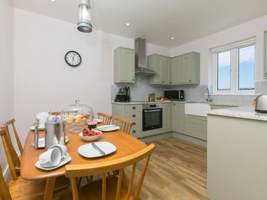 A kitchen with wooden dining table set for tea and green cabinets at Rowena in Mullion