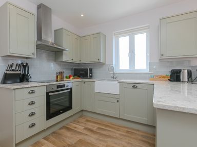 A kitchen with olive green cabinets a built in oven a microwave a white farmhouse sink and a window at Rowena in Mullion