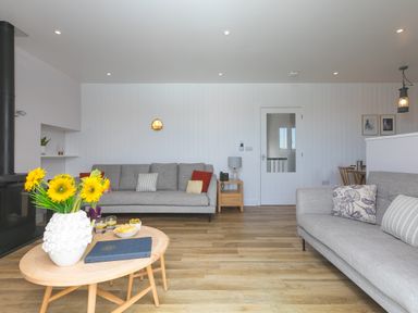 A living room with two grey sofas a wooden coffee table with flowers snacks and drinks at Rowena in Mullion