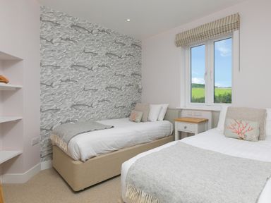 A bedroom with two single beds a window and ocean themed wallpaper at Rowena in Mullion