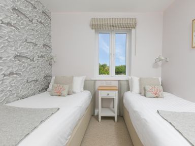 A bedroom with two single beds and a window in the middle at Rowena in Mullion