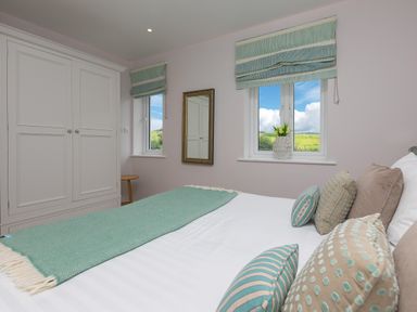 A bedroom with a bed and pillows next to two windows with blinds and a wardrobe at Rowena in Mullion