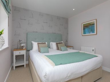 A bedroom with a double bed bedside tables and a painting on the wall at Rowena in Mullion