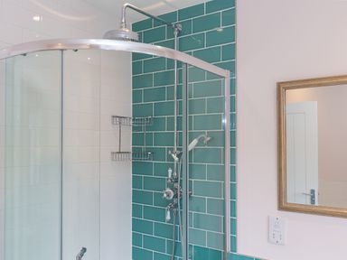 A bathroom shower area with teal and white tiled walls a glass shower enclosure and a mirror on the wall at Rowena in Mullion