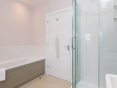 A bathroom with a bathtub shower enclosure and a white door at Rowena in Mullion