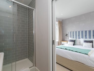 A shower with gray tiles next to a bedroom with a bed and bedside tables at Rowena in Mullion