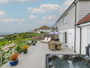 A large outdoor patio with a hot tub dining table with umbrella and lounge chairs overlooking greenery at Morwenna in Mullion