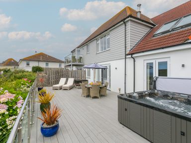 A large outdoor deck with lounge chairs a dining table with an umbrella potted plants and a hot tub at Morwenna in Mullion