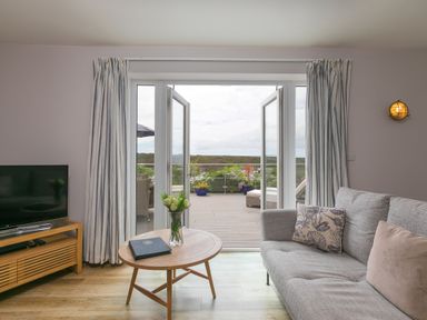 A living room with a sofa coffee table and television with open doors leading to a balcony at Morwenna in Mullion