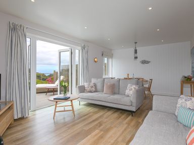 A living room with two sofas a round coffee table and an open door leading to a deck at Morwenna in Mullion