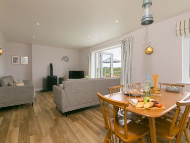 A living room with wood floor sofas a dining table with wine and snacks and a door leading outside at Morwenna in Mullion