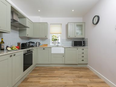 A kitchen with green cabinets a window above a sink and appliances at Morwenna in Mullion