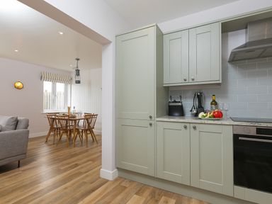 A kitchen with light green cabinets and a wooden dining table with chairs at Morwenna in Mullion