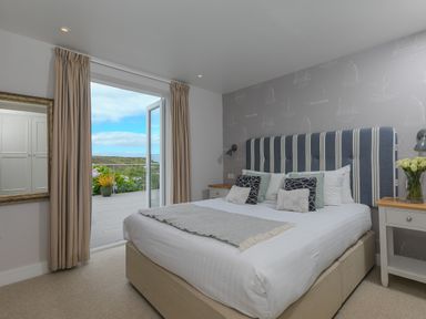 A bedroom with a double bed and striped headboard next to an open door leading to a balcony at Morwenna in Mullion