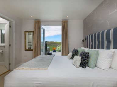 A bedroom with a bed and pillows facing an open door to a balcony with a view at Morwenna in Mullion