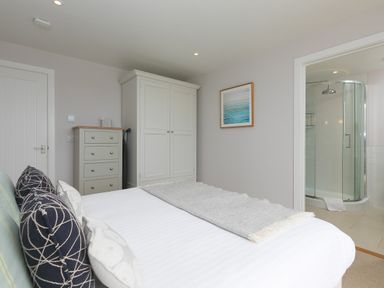 A bedroom with a bed pillows chest of drawers wardrobe and an ensuite bathroom at Morwenna in Mullion