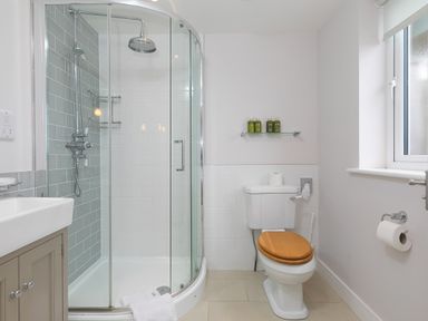 A bathroom with a shower enclosure, toilet with a wooden seat, sink, and a window at Morwenna in Mullion