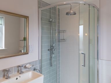 A bathroom with a glass shower enclosure tiled walls and a sink with a mirror at Morwenna in Mullion