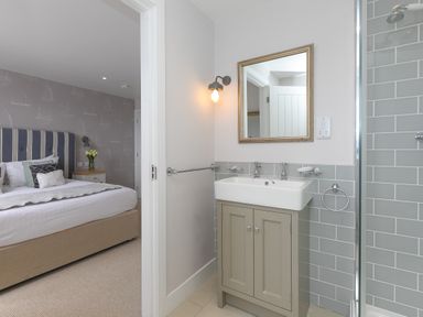 A bathroom with a sink cabinet mirror and shower visible next to a bedroom with a bed and bedside table at Morwenna in Mullion