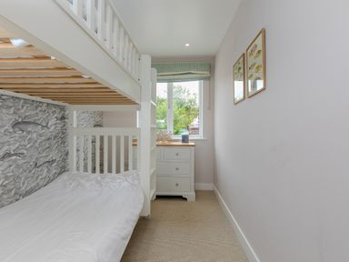 A small bedroom with a white bunk bed white dresser under a window and fish pictures on the wall at Morwenna in Mullion