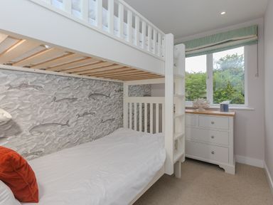 A bedroom with a white bunk bed, a chest of drawers under a window, and a wallpaper with sea creatures at Morwenna in Mullion
