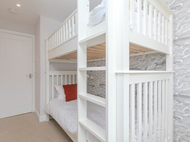 A bedroom with a white bunk bed and red pillow and a door at Morwenna in Mullion
