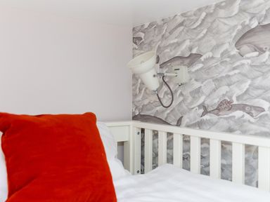 A bed with a red pillow and white bedding next to a white wall lamp and a wall with ocean animal wallpaper at Morwenna in Mullion