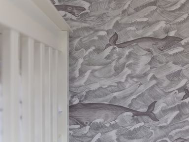 A close up of a white railing next to a wall with a wallpaper pattern of whales in the ocean waves at Morwenna in Mullion