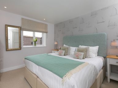 A bedroom with a bed with green throw and boat patterned wallpaper at Morwenna in Mullion