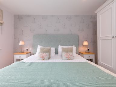 A bedroom with a double bed two bedside tables with lamps and a wardrobe at Morwenna in Mullion