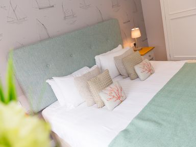 A bed with a light green headboard white linens and decorative pillows next to a nightstand with a lamp and a door in the background at Morwenna in Mullion