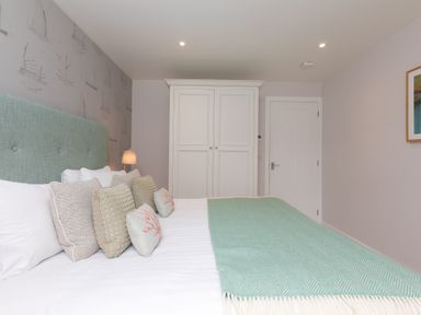 A bedroom with a bed with pillows and a turquoise blanket a white wardrobe and a door at Morwenna in Mullion