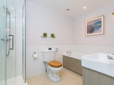 A bathroom with a shower, toilet with wooden seat, bathtub, sink, and framed artwork at Morwenna in Mullion
