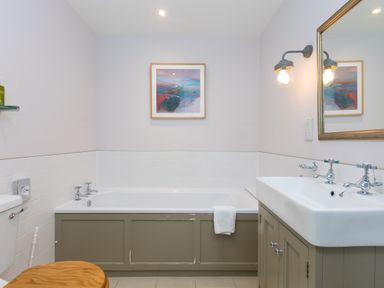 A bathroom with a bathtub towel sink mirror light and a toilet with a wooden seat at Morwenna in Mullion