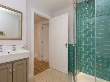 A bathroom with a sink and mirror on the left and a glass shower enclosure with green tiled walls on the right at Morwenna in Mullion