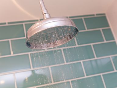 A shower head with water running in a bathroom with green rectangular tiles at Morwenna in Mullion
