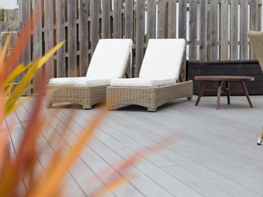 Two wicker lounge chairs with white cushions on a wooden deck with a small round wooden table and wooden fence in the background at Morwenna in Mullion