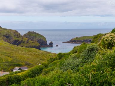 A coastal landscape with rocky cliffs green vegetation and a few buildings near the sea at Morwenna Mullion