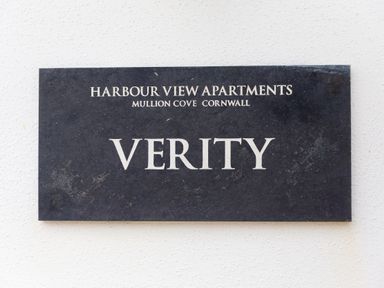 A black sign with white text reading Harbour View Apartments Mullion Cove Cornwall Verity