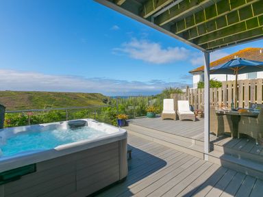 An outdoor deck area with a hot tub two lounge chairs dining table with chairs and an umbrella at Verity in Mullion