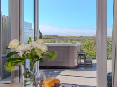 A view through glass doors to an outdoor hot tub on a deck with a flower vase in the foreground at Verity in Mullion