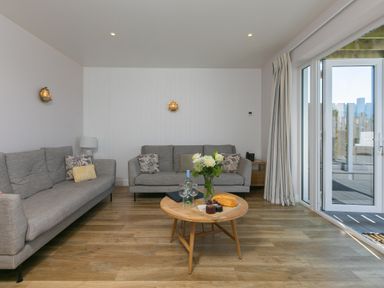 A living room with two gray sofas a round wooden coffee table with flowers bread and wine glasses and sliding glass doors at Verity in Mullion