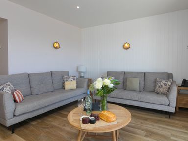 A living room with two gray sofas a round wooden coffee table with flowers bread and wine at Verity in Mullion
