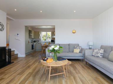 A living room with gray sofas and a round wooden coffee table with flowers and bread visible at Verity in Mullion